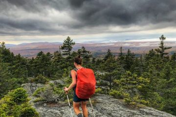 Heather Anderson walks with a heavy pack across a bald mountain with stormy skies in the distance