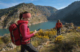 A woman looking at her Garmin GPSMAP 66i device in the backcountry, with an aqua-blue lake in the background