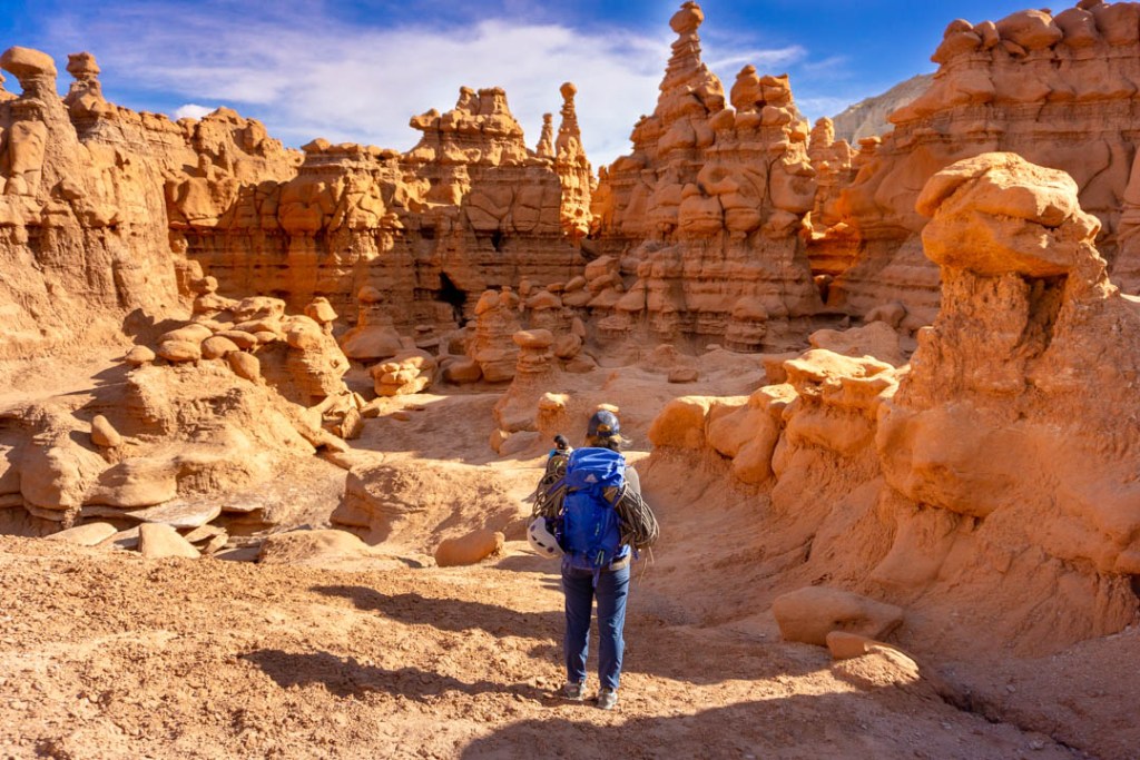 A climber walks toward red towards, rope strapped to their back.