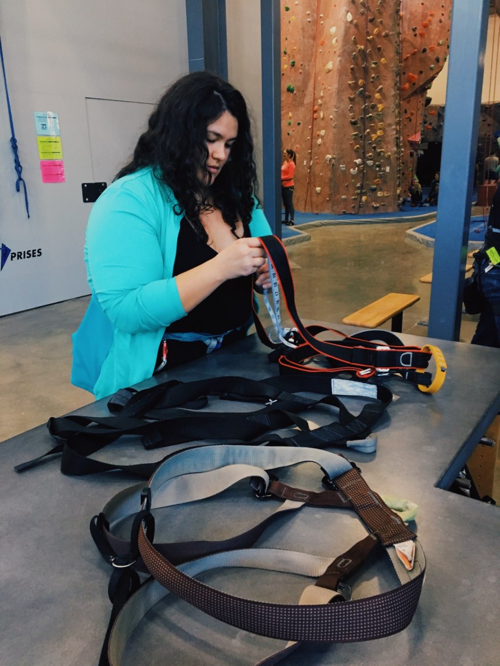 Sam Ortiz inspects climbing harnesses sitting on a counter at Edgeworks Climbing in Tacoma, Wash.