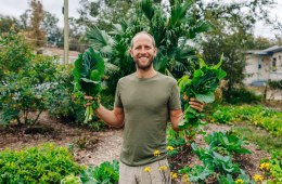 Rob Greenfield in a garden holding green leafy vegetables.