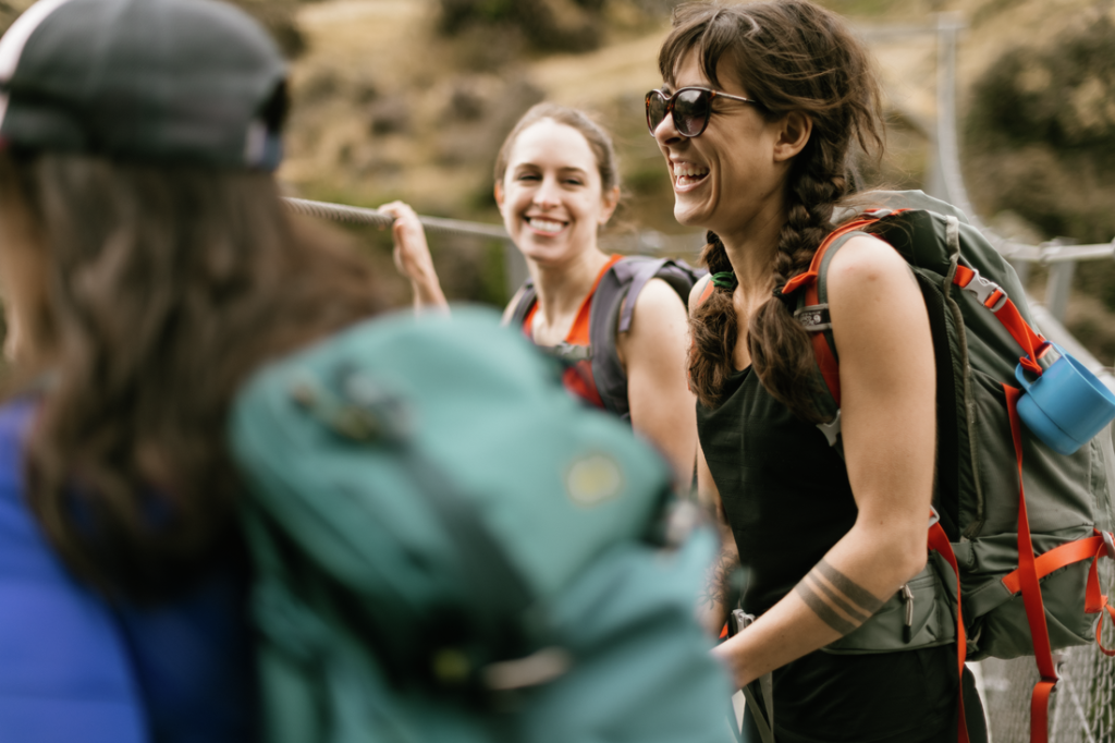 A group of backpackers laughs, one with sunglasses on is in the front.