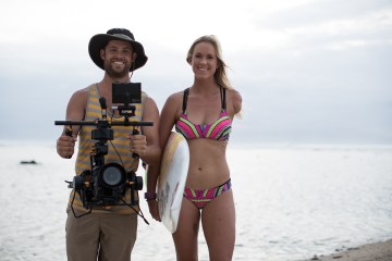 Aaron, the director of Unstoppable, standing next to Bethany Hamilton who is carrying a surfboard.