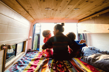 A mom snuggles with her two kids in a van