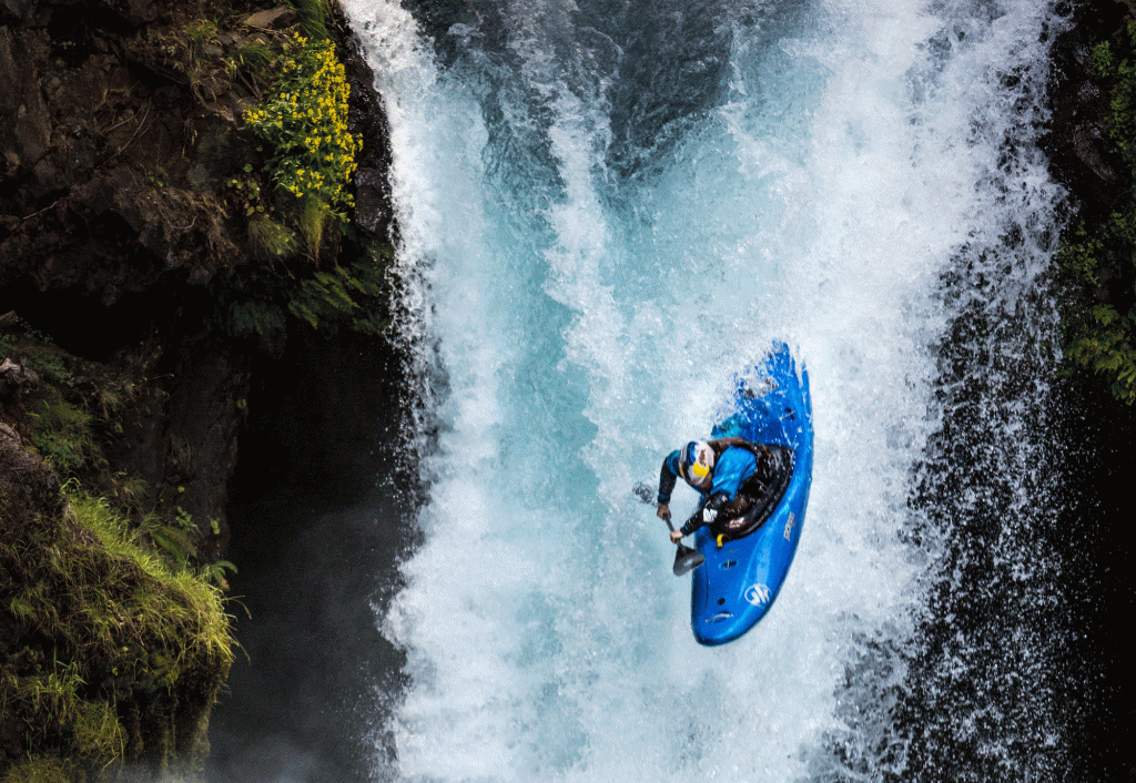 A kayaker descends a rushing waterfall with greenery and rocks along the outside