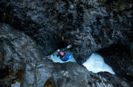 A kayaker drops into a light-blue pool amid jagged rocks