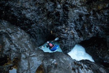 A kayaker drops into a light-blue pool amid jagged rocks