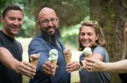 Four people smile and cheers their ice cream in cones.