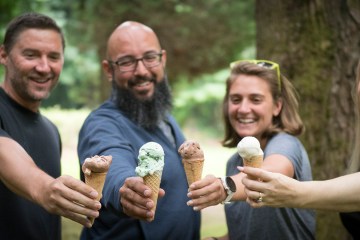 Four people smile and cheers their ice cream in cones.