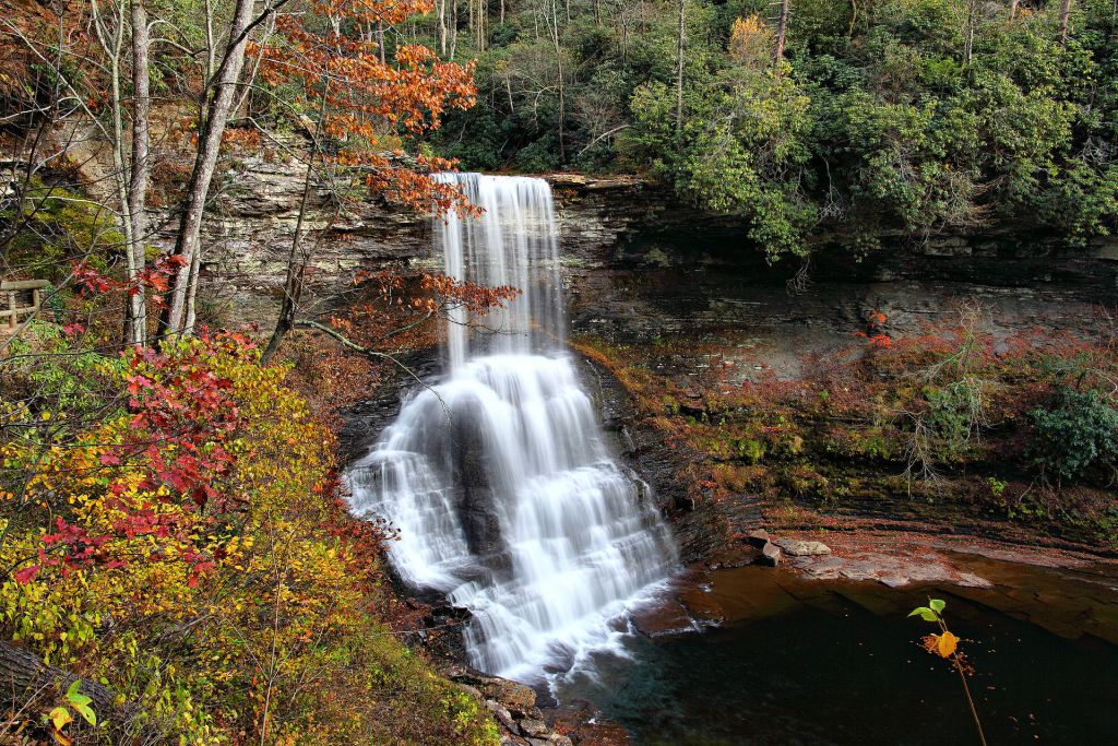 Rushing water falls into a deep pool surrounded by fall foliage 
