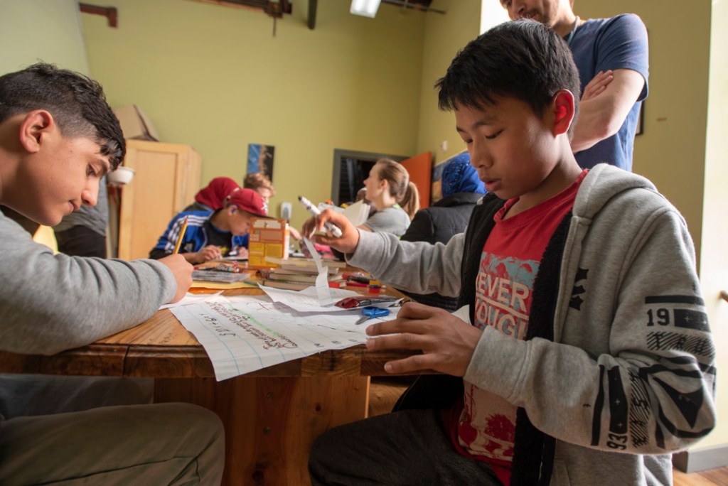 Swee Mana sits at a table, using a marker and scissors to work on a non-climbing project.