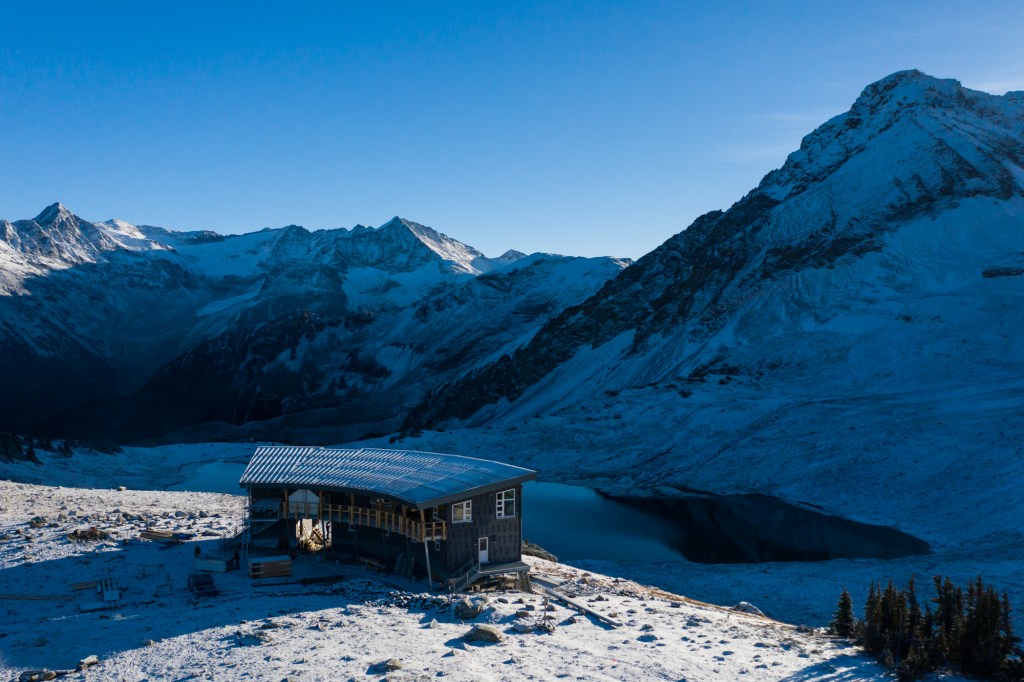The Kees and Claire Hut is at the edge of a lake and the base of a jagged peak.