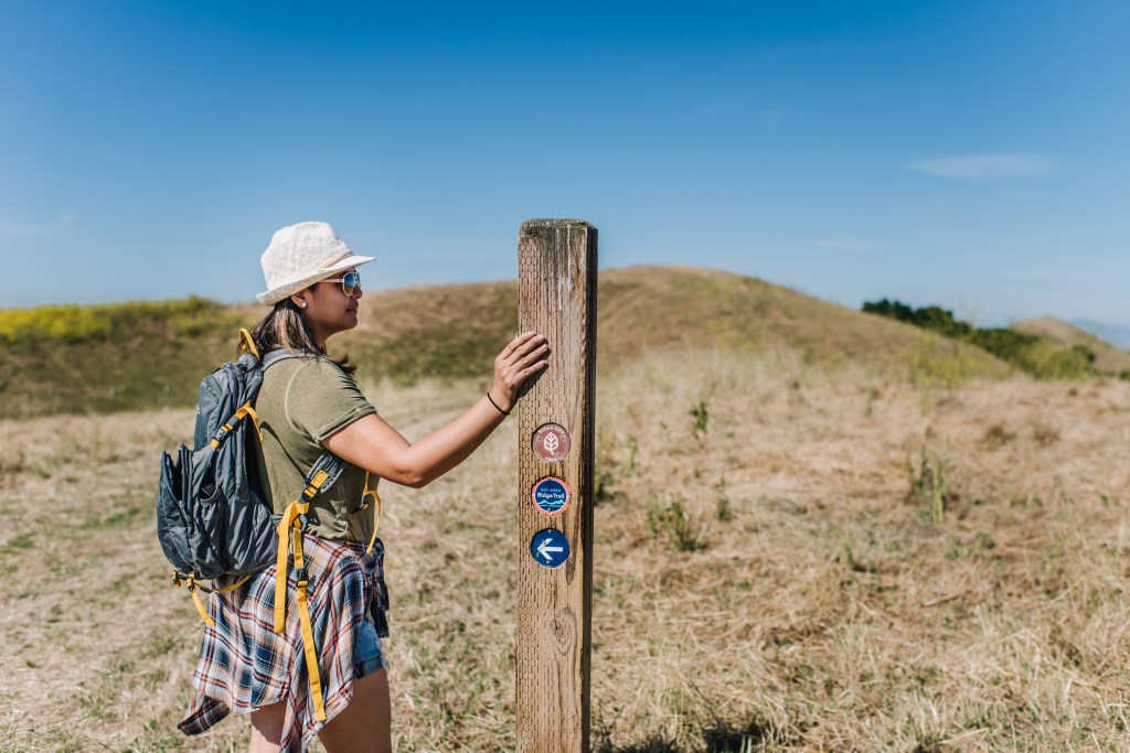 Hiker touching a wooden post with a trail marker on it.