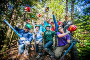 A trail crew celebrates the end of a hard day's work surrounded by leafy green trees