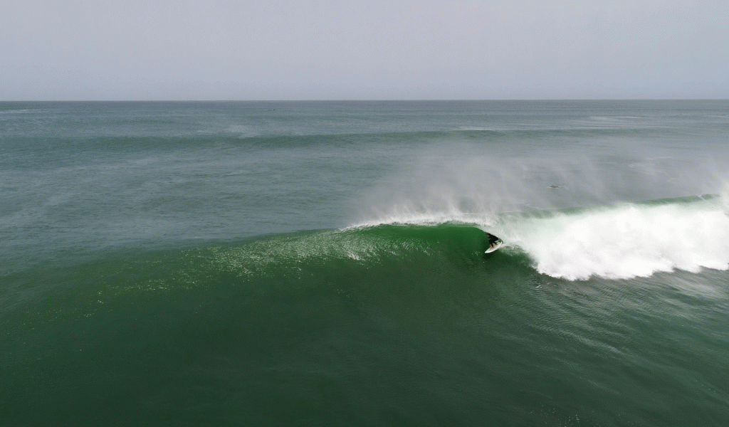 A surfer gets barreled in a wave amid a blue-green sea with a grey sky in the background