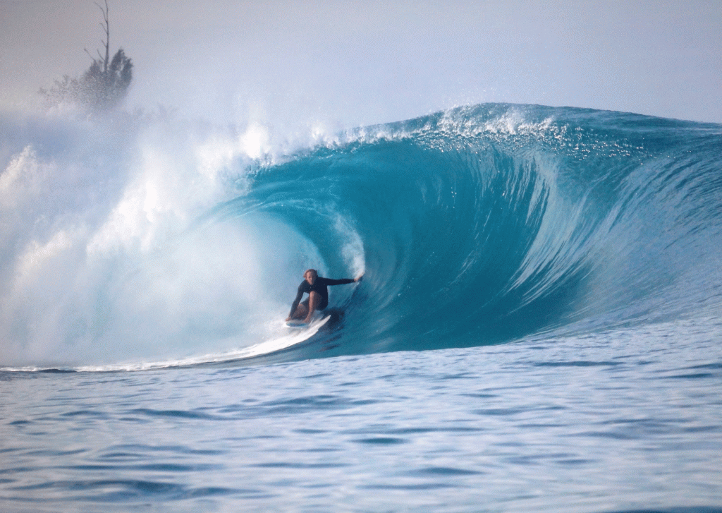 A surfer gets barreled in a turquoise-blue wave
