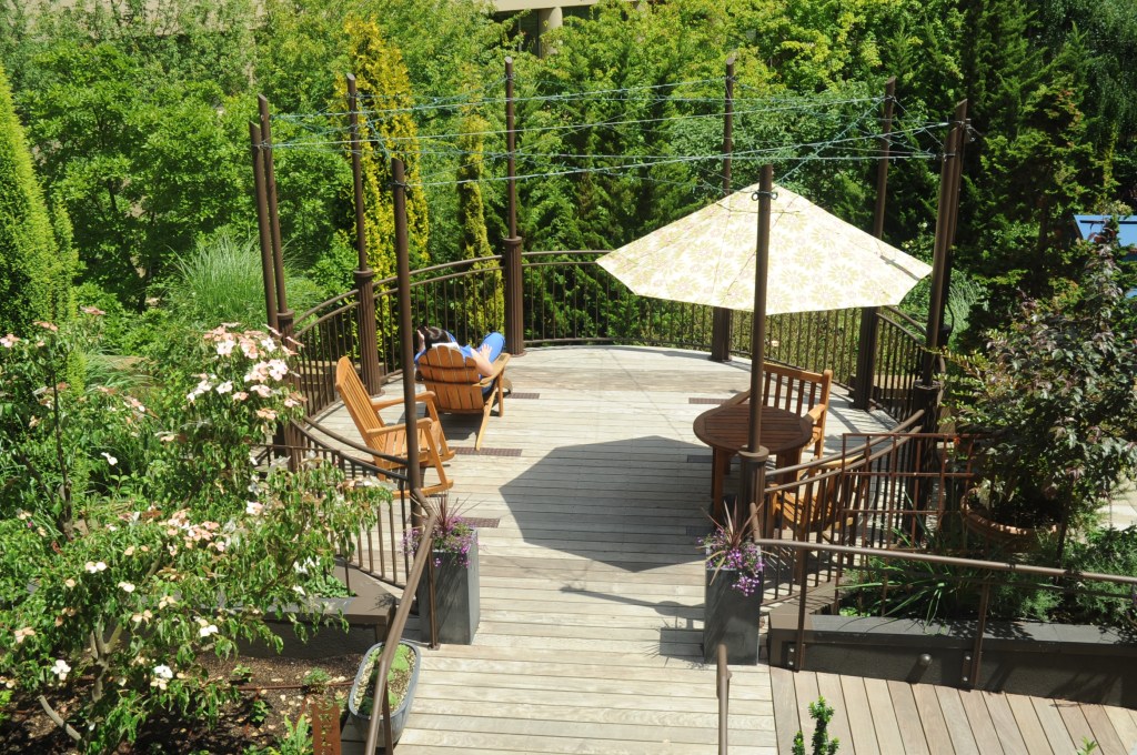 A deck with seating and an umbrella looks out over lush green trees.