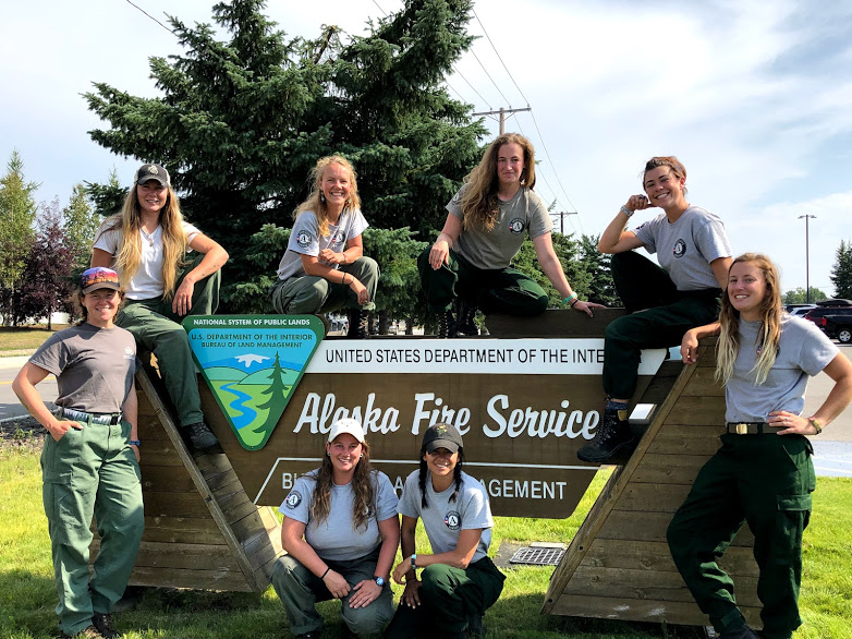 Women pose in front of a sign in Alaska