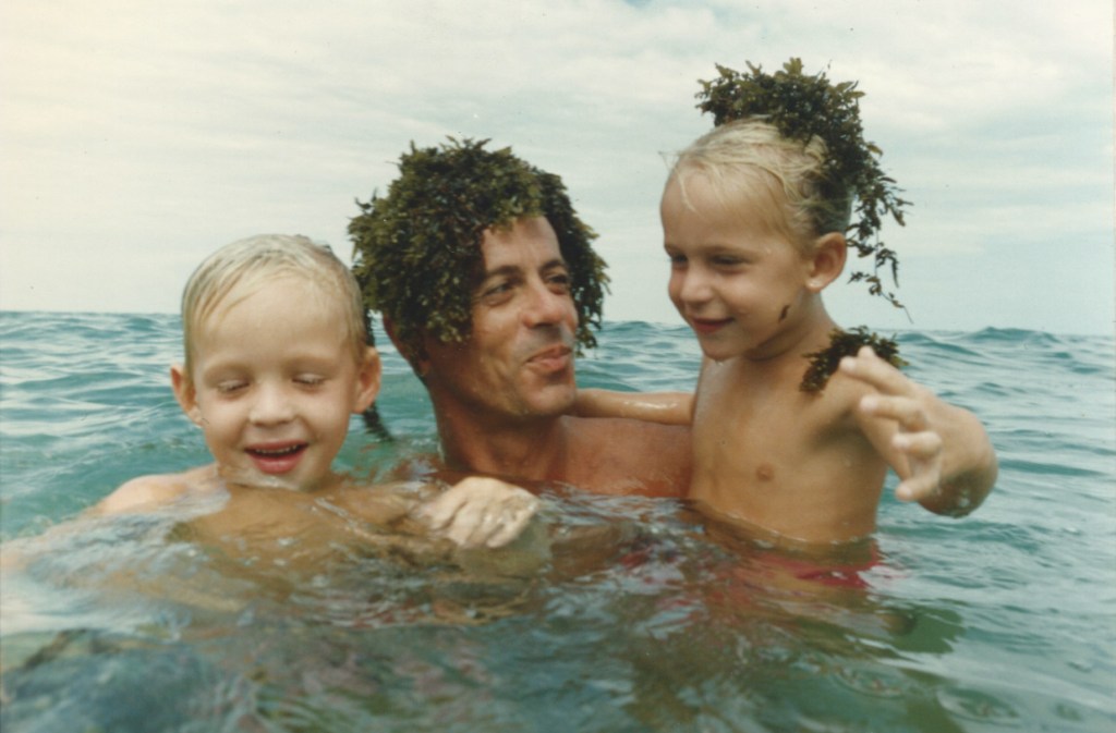 Two young boys play in the water with seaweed and their dad
