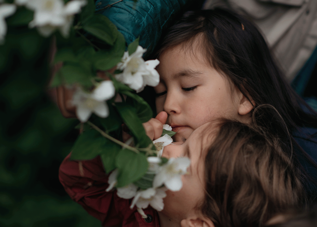Two young girls breathe in the scent of white flower blossoms