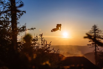 a mountain biker in mid-air from a jump with a sunset in the background at snowshoe, west virginia