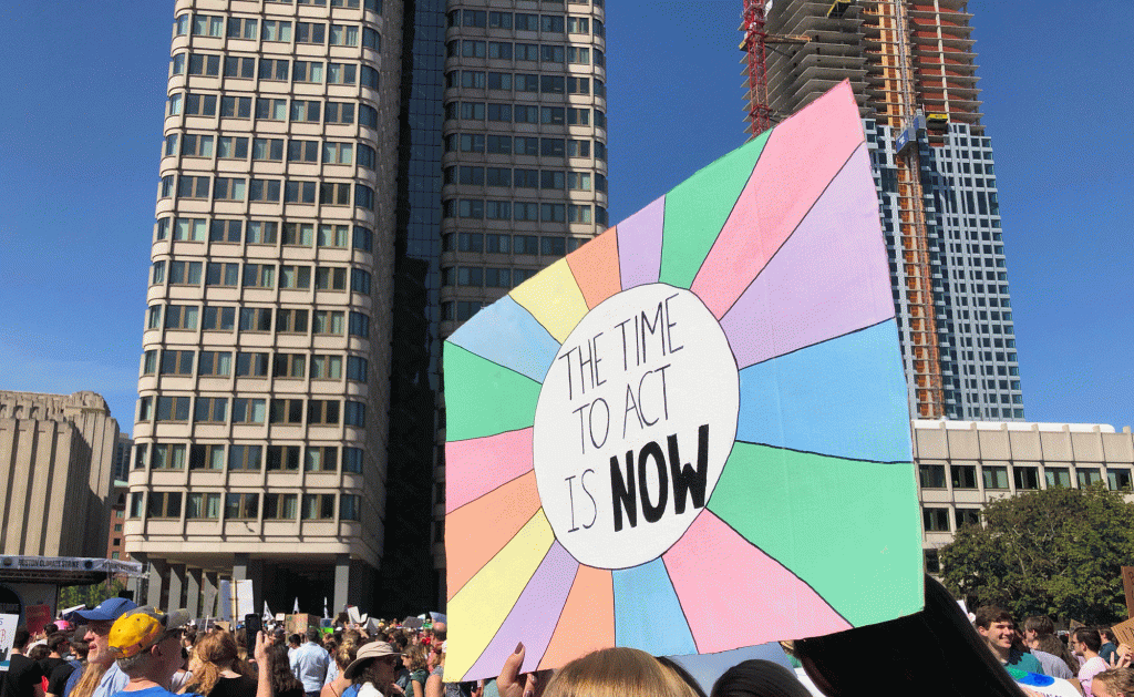 A colorful sign bearing the message "The Time to Act Is Now"