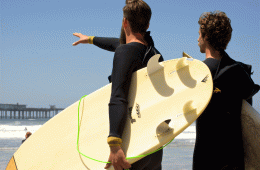 Two surfers stare out at a surf break under a blue sky