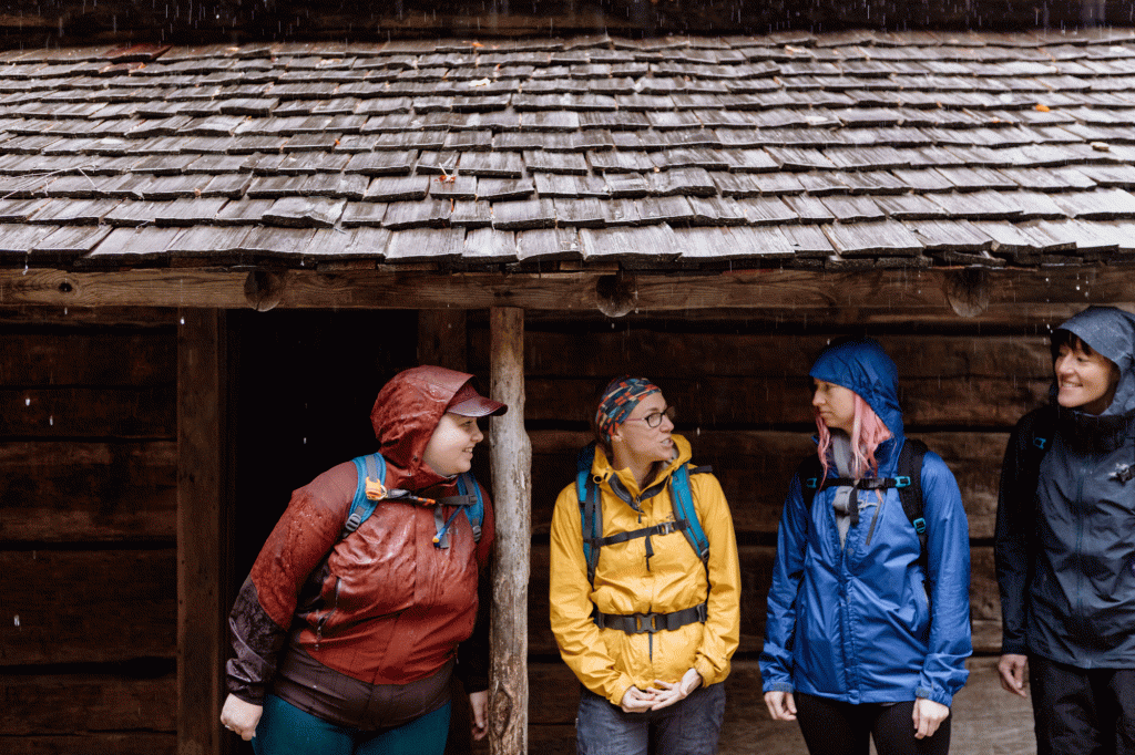 Recreationists in full rain gear chat with each other inside a shelter 