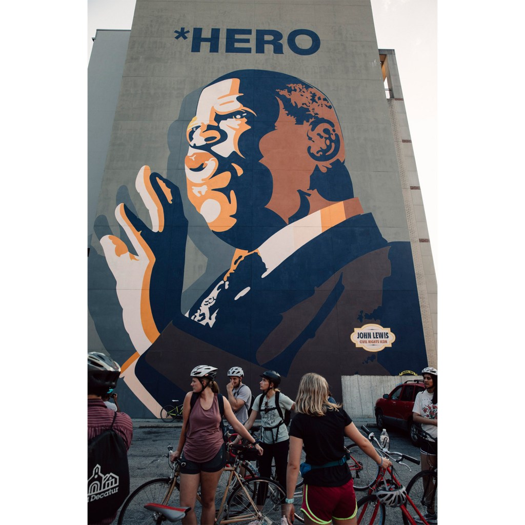Bike riders pause for a breadth beneath a mural of Rep. John Lewis