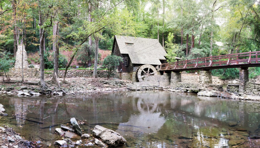 A wood and stone bridge crosses a creek to a mill house. 