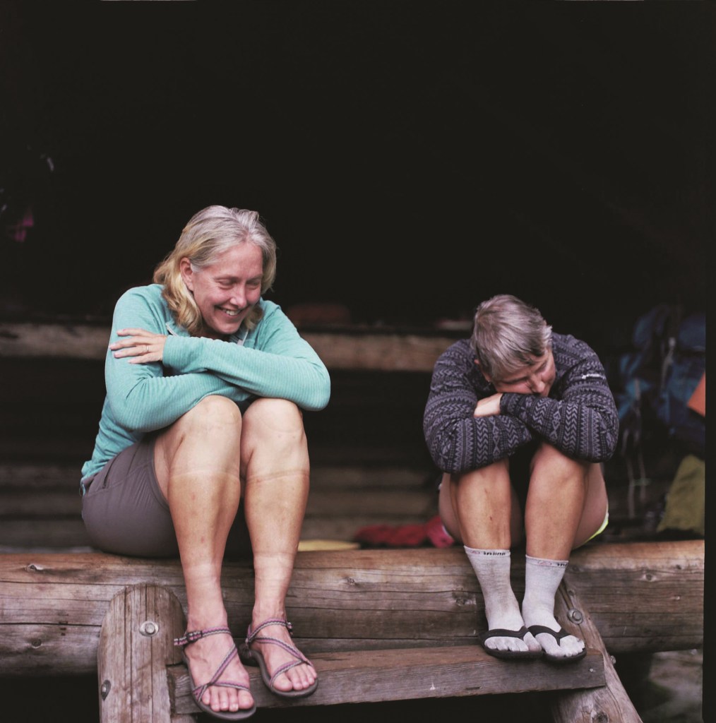 Two thru-hikers sit in a shelter, laughing.