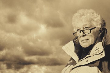 A woman wearing a sports jacket peers into the horizon with storm clouds behind her