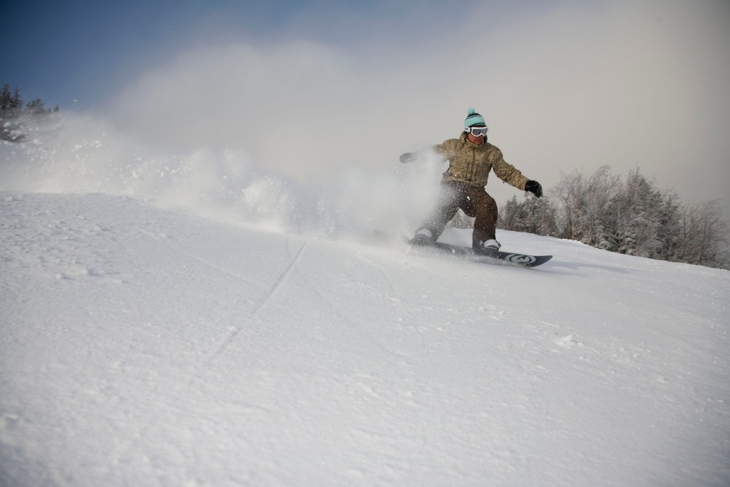 A snowboarder slices through powder under a cloudy blue sky