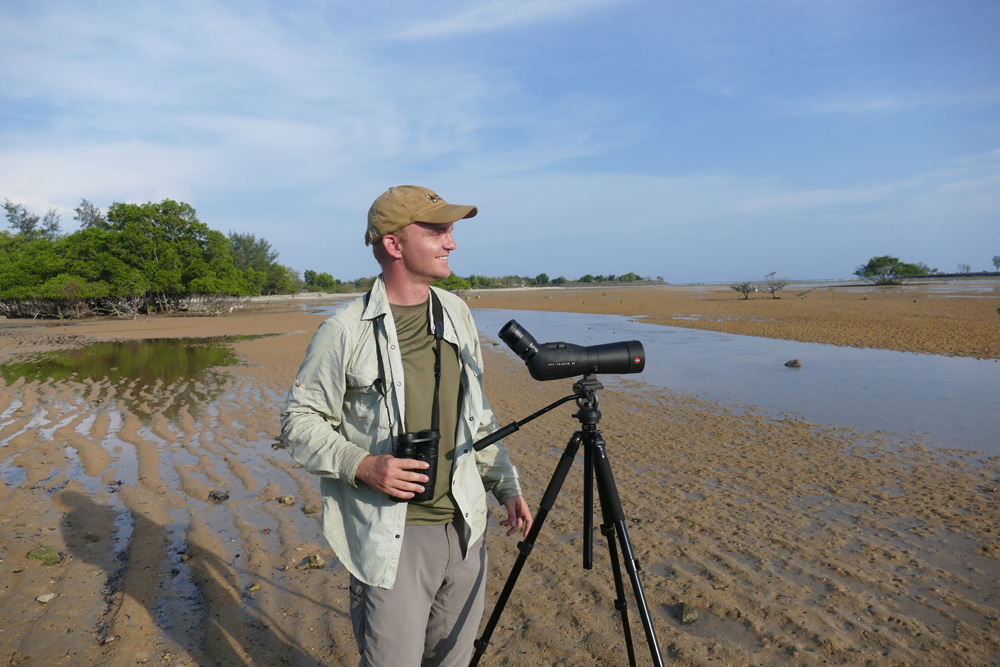 A man stands with a telescope on a beach in Bali