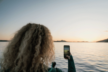 A woman snaps a photo of a beautiful seascape at dusk
