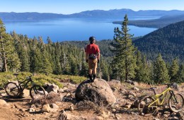 A person stands on a rock overlooking Lake Tahoe near a mountain bike trail