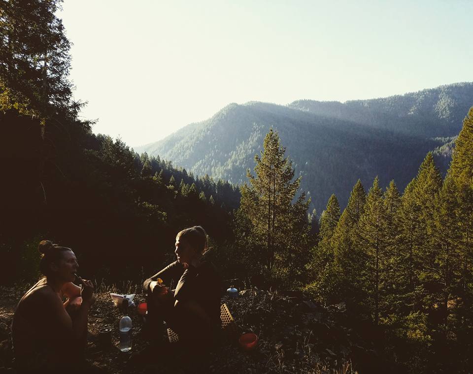 Three friends enjoy breakfast in the mountains surrounded by fir trees