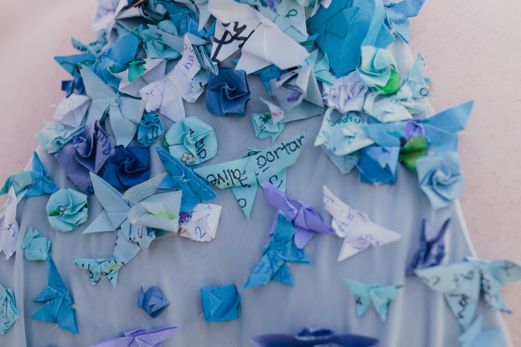 Paper with writing on it is folded elegantly and attached to a dress.