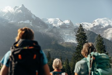 Three people look out on snow-covered peaks in the French Alps.