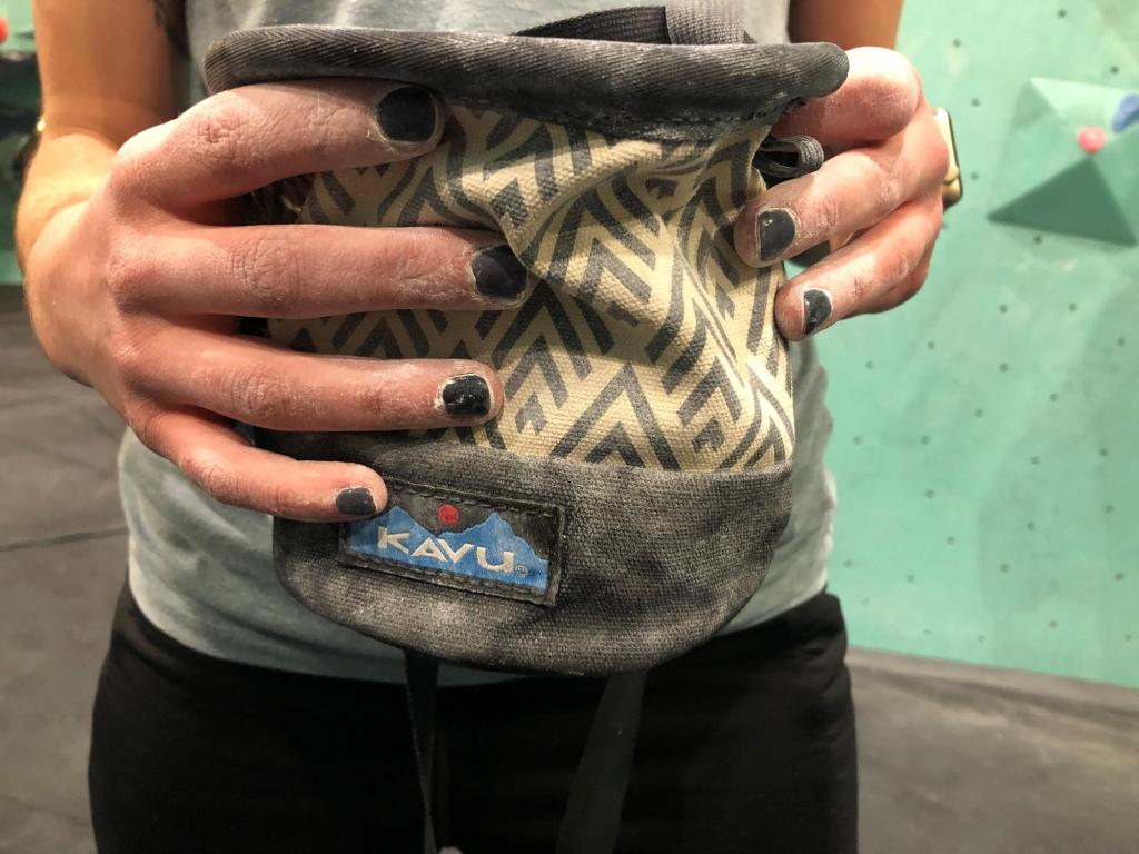 Two hands with black nails holding a KAVU bag.