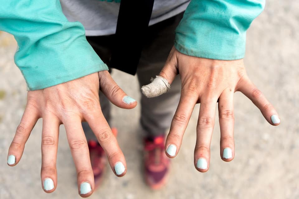 Climber with light blue nails stretched out and a wrap on one thumb.