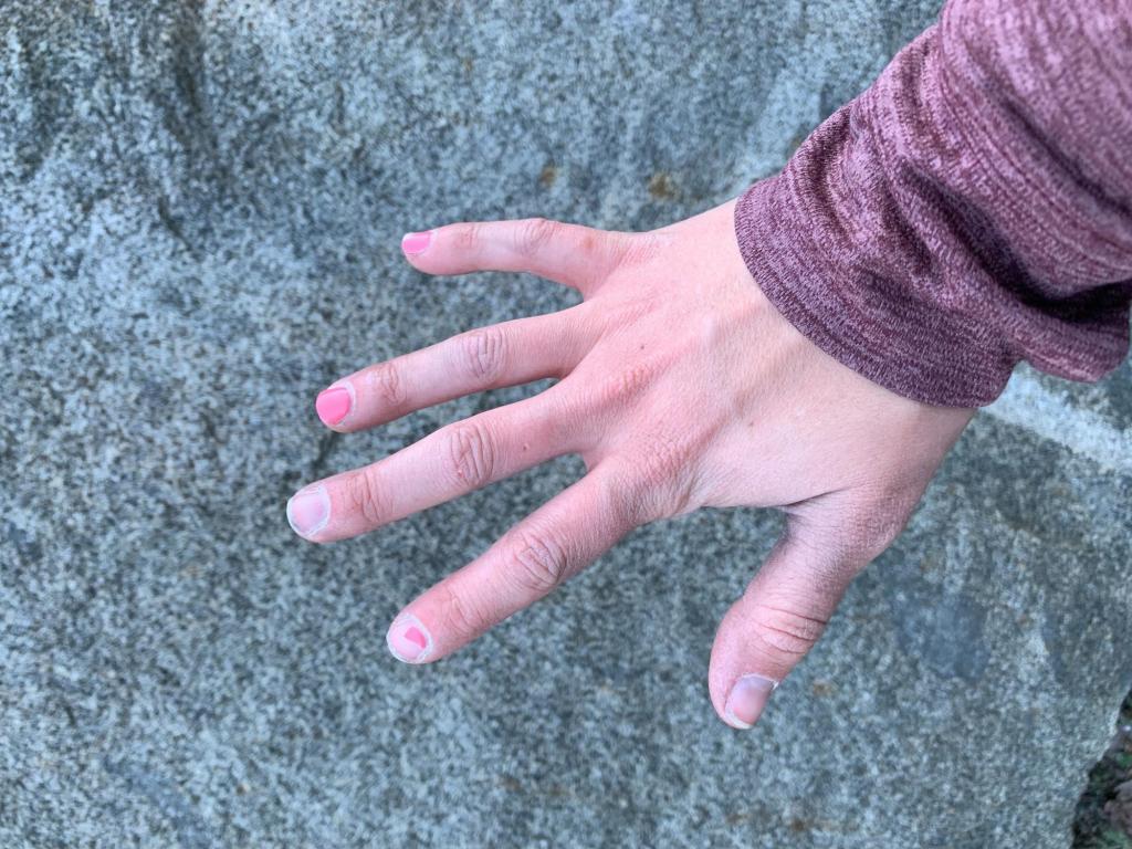 One hand stretched out in front of a rock, wearing chipped pink paint.