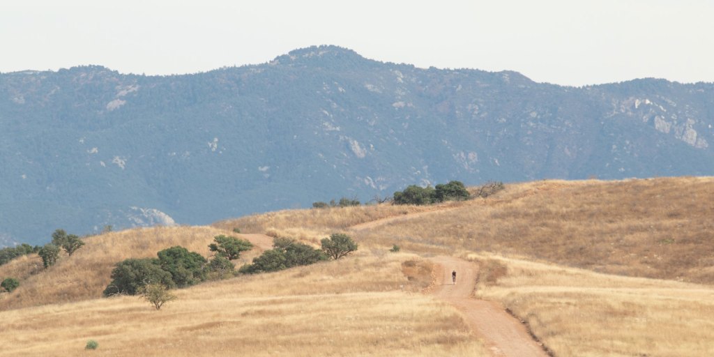 A cyclist rides with mountains in the distance. 