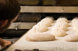 Eric Wolfinger putting unbaked loaves of bread into an oven.