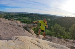 Joe Gray, wearing a green shirt and black shorts, is running up a rocky trail.