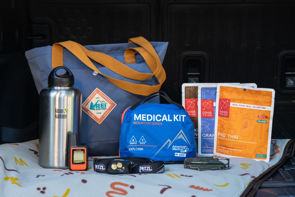 Picture of dehydrated food, a water bottle, an REI tote and a medical kit.