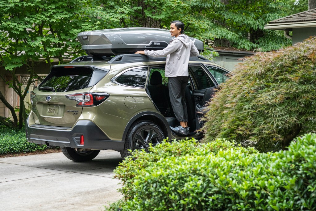 Woman checking the cargo box strapped to the top of her Subaru.