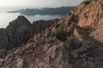 Two runners jogging across a trail at the edge of the mountains.
