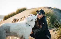 Ally Coucke is kneeling on the beach with her two dogs kissing her face.