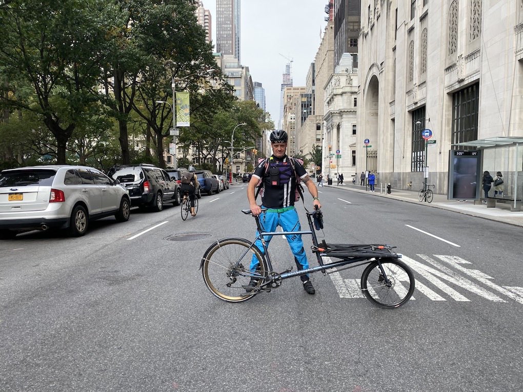 Cyclist standing behind bike in street.